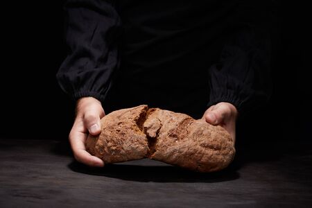 So, break bread with me. Cropped view of male Chef breaking freshly Baked Sourdough Bread, focus on loaf of bread.の写真素材
