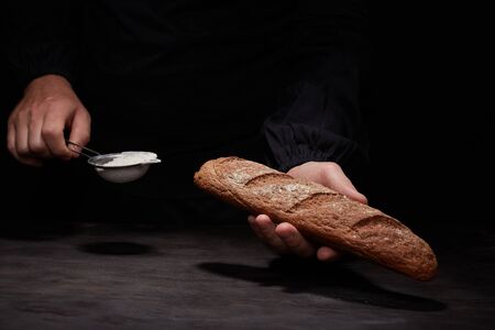 baked oval rye bread in sprinkles of white flour, black backgroundの写真素材