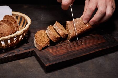 The woman's hand or chef cut with a knife, a loaf of white bread, loaf or baguette in slices, on a...