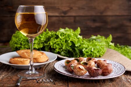 Escargots de Bourgogne - Snails with herbs butter on wooden background. Salad. Parsley. Glass of wine.の写真素材