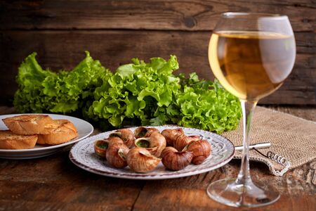 Escargots de Bourgogne - Snails with herbs butter on wooden background. Salad. Parsley. Glass of wine.の写真素材