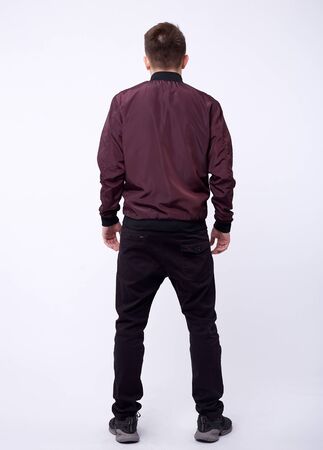Young man in jeans, shiny nylon burgundy bomber jacket on white background.の写真素材