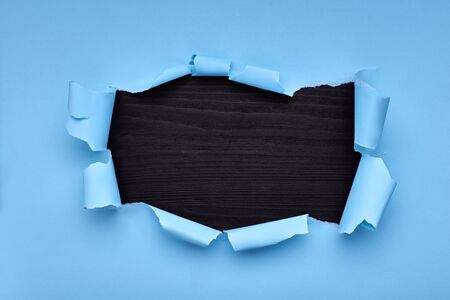 Hole in the blue paper. Torn. Black wooden background. Abstract backgroundの写真素材