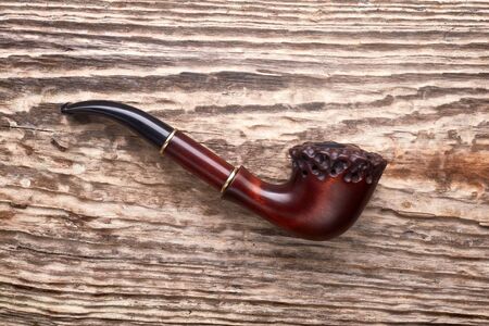 Tobacco pipe on old wooden background.