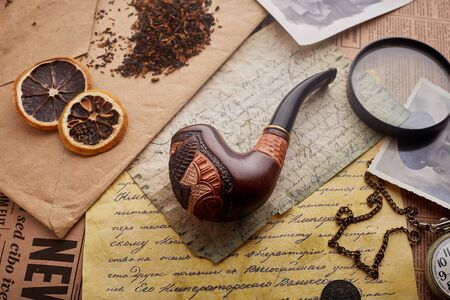 Tobacco pipe on old wooden background. Vintage letters, watches, coins and tobacco, slices of dried...