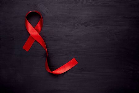 AIDS disease. Red ribbon on black wooden background, top view, copy space.の写真素材