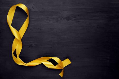 Golden, yellow ribbon bow on black wooden background. Copy space.の写真素材