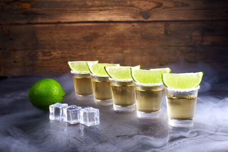 Mexican tequila gold in short glasses with salt, lime slices and ice on a wooden table. Smoke.の写真素材