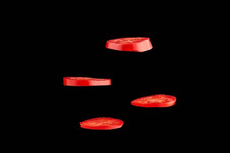 Creative concept with flying tomato. Sliced red tomato isolated on black background. Levity vegetable floating in the airの写真素材