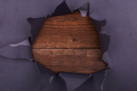 Big hole in the black paper. Torn. Wooden background. Abstract background.の写真素材