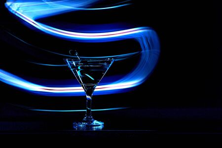 Martini cocktail drink splash with ice cubes in neon iridescent . Minimal night party life concept.の写真素材