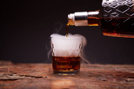 Glass of whiskey on wooden table. Pouring whiskey, smoke.の写真素材