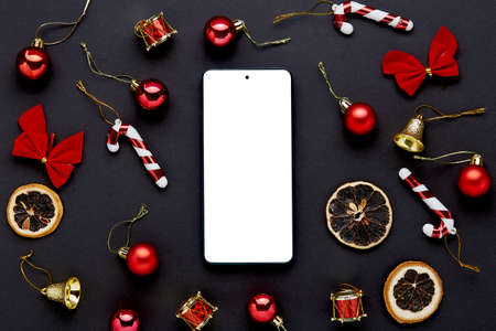 Mobile phone with empty screen on black table. Christmas decoration.