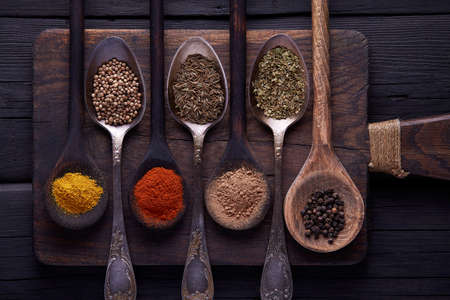 Cutting board with spices and herbs for cooking meat on dark background