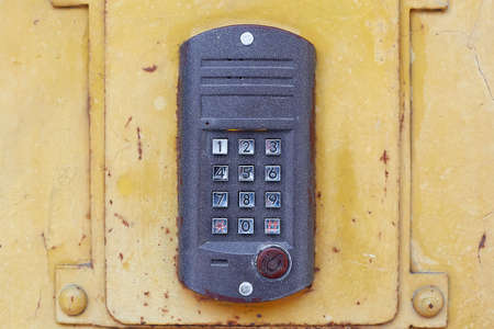 A dark intercom with round buttons and a dial on a metal door.