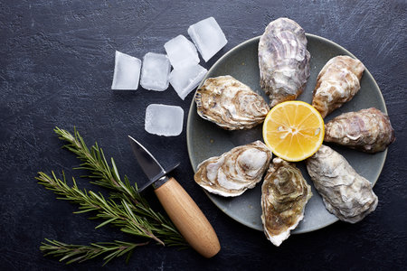 Fresh closed oysters, ice and lemon on a round plate, stone textured background.の写真素材