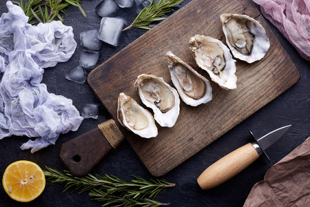 Fresh opened oysters, ice and lemon on a round plate, stone textured background.の写真素材