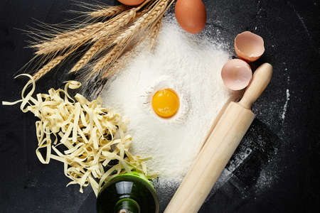 Homemade raw noodles made from flour, egg on wooden bowl on blackの写真素材