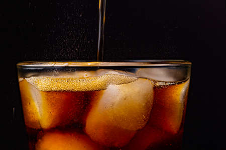 Fizz sparkling cola water refreshing bubbly soda pop with Ice cubes. Glass of cola on black background closeup.の写真素材