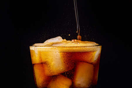 Fizz sparkling cola water refreshing bubbly soda pop with Ice cubes. Glass of cola on black background closeup.の写真素材