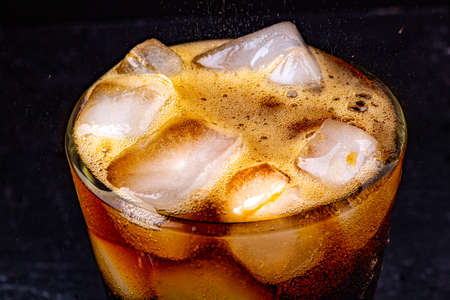 Fizz sparkling cola water refreshing bubbly soda pop with Ice cubes. Glass of cola on black background closeup.の写真素材