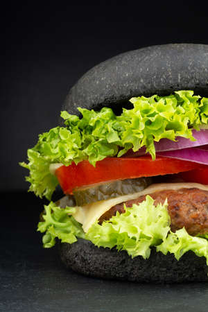Black burger with cheese. Cheeseburger with black bun on dark backgroundの写真素材