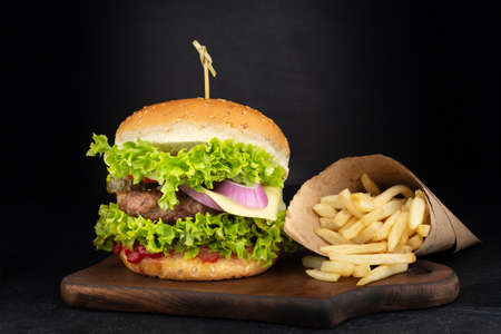 Big single cheeseburger with french fries on dark backgroundの写真素材