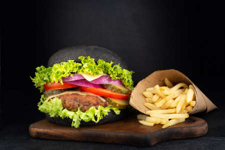 Big single cheeseburger with french fries on dark backgroundの写真素材