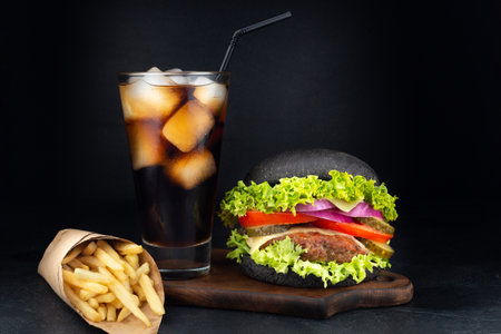 Big single cheeseburger with glass of cola and french fries on dark backgroundの写真素材