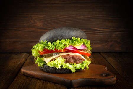 Fresh homemade burger on little wooden cutting board over dark background.の写真素材