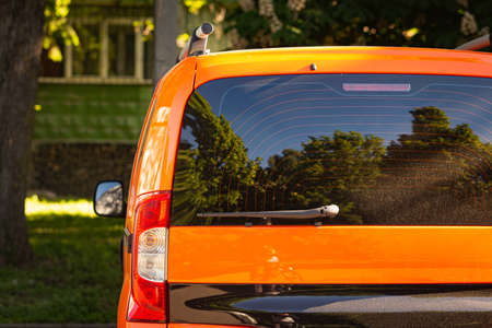 Back window of orange car parked on the street in summer sunny day, rear view. Mock-up for sticker...