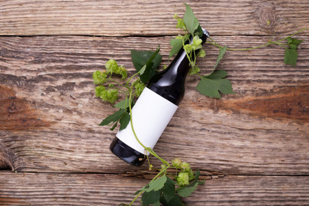 Beer bottle lies on wooden background with hop cones, close up. White label mock upの写真素材