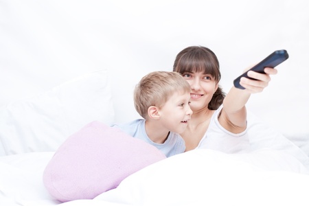 Mother with remote control and son lying on the bed and watching TVの写真素材