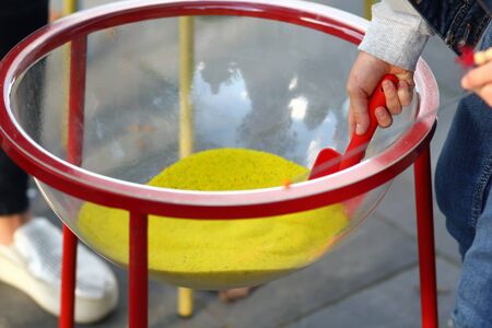Closeup of child's hand with a shovel taking yellow colorful sand out of a plastic bowl. Art therapy