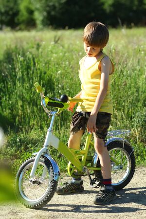 Candid portrait of an upset boy with a bicycle in the sunlit summer fieldの写真素材