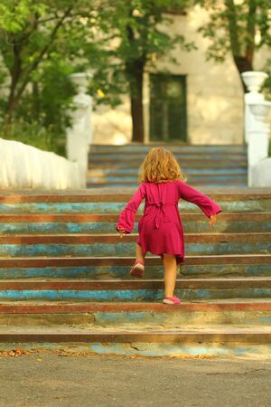 Purposeful toddler girl in pink dress reaching the top of old blue vintage stairsの写真素材