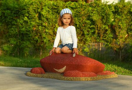 Cheerful toddler girl on the sunlit summer playground in the park. White t shirt mock upの写真素材