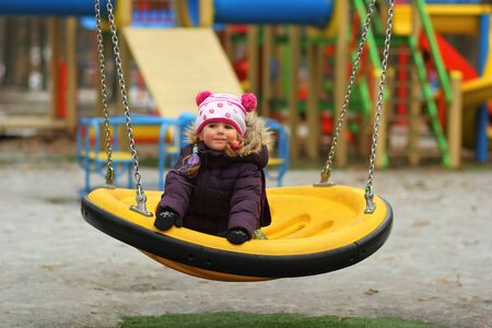 Portrait of dreaming three year old toddler girl with colorful braided hair, swinging outdoorsの写真素材