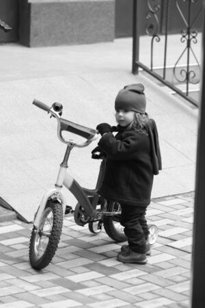 Candid street portrait of a cute two year old toddler girl dreaming of riding elder brother's bikeの写真素材