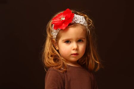 Portrait of cute two year old toddler with a red flower headband, isolated on blackの写真素材