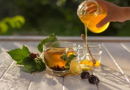 Healthy breakfast concept. Tea with lemon, berries and honey in a jar. Woman is pouring honey.の写真素材