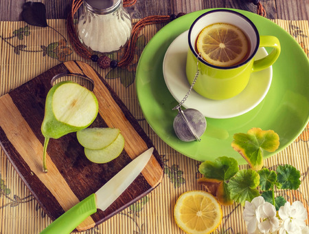 Healthy breakfast. Tea with lemon in a green cup. Near the sugar bowl, a board with a green pear and a knife. Atmospheric photo. Fresh bright colors. Top view.の写真素材