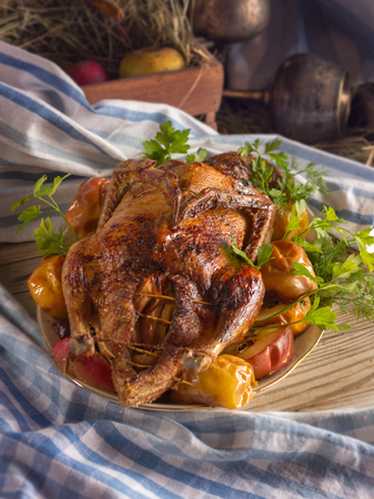 Christmas duck in apples on a plate. Christmas dinner. The wooden stor is decorated with cloth napkins. In the background is a basket with hay and wine glasses.の写真素材
