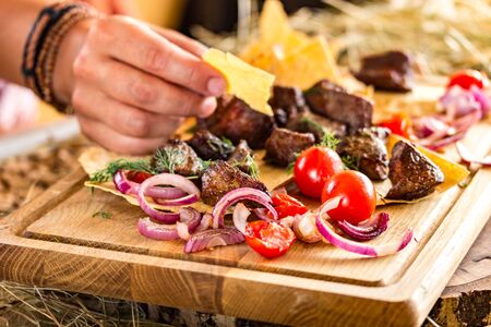 slices of fried meat with onions and cherry tomatoes on a thin flat cake. Female hand takes a piece of cake. Horizontal, bright colors, space for textの写真素材
