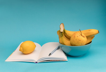 Fruit in a bowl with notebook and pen on a blue backgroundの写真素材