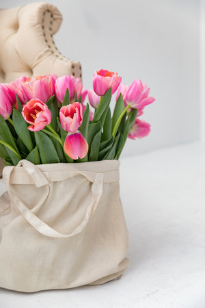 Pink tulips in a canvas bag next to the sofa in a bright interior. Copy spaceの写真素材