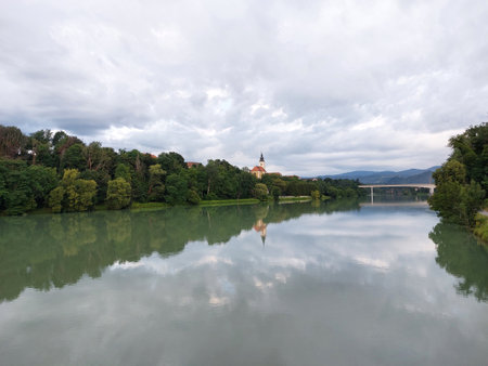 green trees and church are reflected in river Drava in Maribor. Europe. Overcast. Summerの写真素材