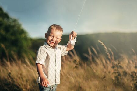 little white-haired boy laughs in sunny summer weather outdoors and holds a paper plane in his handsの写真素材