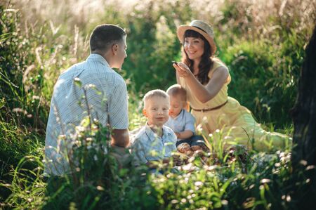 dad and mom with young children are sitting on the grass on a picnic and laughingの写真素材