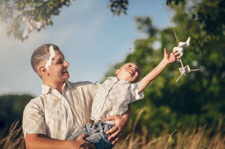father holds his son in his arms on the street in sunny weather and plays with paper planesの写真素材